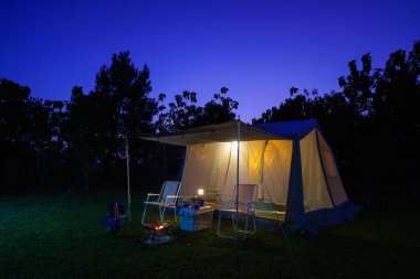 Geceleri kamp çadırları, antika kulübeler, antika gaz lambaları, retro sandalyeler ve ormandaki kamp alanındaki masalarda açık kahve yapma tesisleri olan bir grup kamp çadırı.
