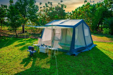 Sabahları yeşil çimenlerin üzerinde kamp çadırları, eski kulübe çadırları, antika gaz lambaları, retro sandalyeler, açık hava kahve yapma tesisleri ormandaki bir kamp alanındaki masaların üzerinde.