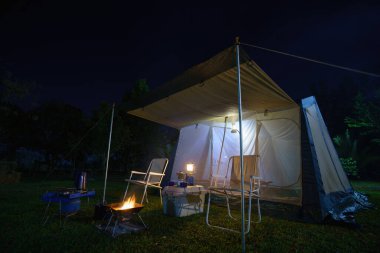 Geceleri kamp çadırları, antika kulübeler, antika gaz lambaları, retro sandalyeler ve ormandaki kamp alanındaki masalarda açık kahve yapma tesisleri olan bir grup kamp çadırı.