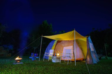 Geceleri yeşil çimlerin üzerinde kamp çadırı, antika gaz lambaları, retro sandalyeler, ormandaki kamp alanındaki masalarda açık kahve yapma tesisleri.