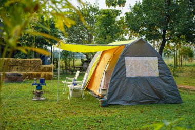 Sabahları yeşil çimlerin üzerinde kamp çadırı, antika gaz lambaları, retro sandalyeler, ormandaki kamp alanındaki masalarda açık kahve yapma tesisleri.