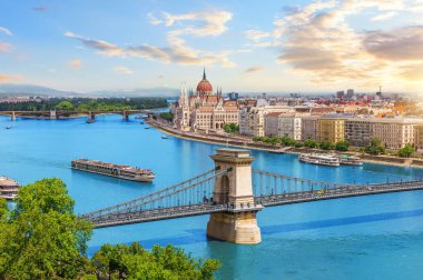 Budapeşte 'deki Zincir Köprüsü ve Parlamento binası, Tuna Nehri manzaralı gün batımında nehir botlarıyla.