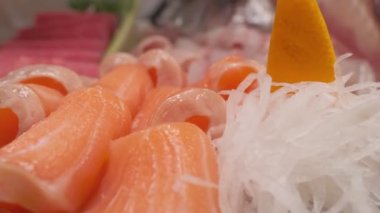 Suşi dekorasyonuna daikon, yapraklar ve kafayla balık kesmek ve siyah kare tabakta farklı türde kırmızı balık dilimleri koymak. Yakın çekim.