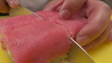 Making sushi rolls. Chief is cutting ready two sushi roll at once using chiefs knife. Closeup.