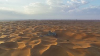 The flight of a drone around a lonely rock among the sandy desert against the backdrop of sunset