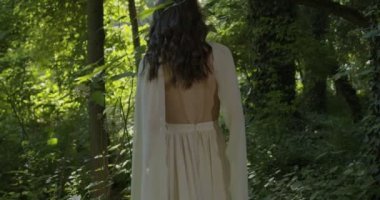 A young girl runs through a summer flowering garden among the trees in a light white fluttering dress. Slow motion