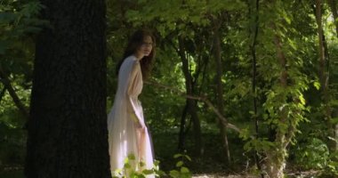 A young girl runs through a summer flowering garden among the trees in a light white fluttering dress. Slow motion
