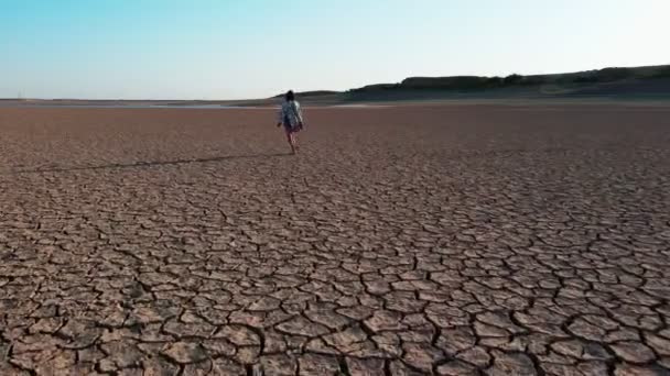 ショートパンツと開発シャツで乾燥した湖の女の子に沿って歩く無人機からの撮影 — ストック動画