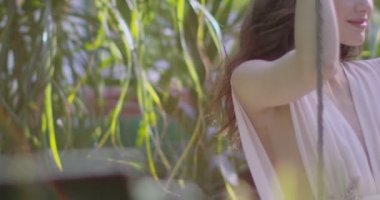 A young beautiful woman in a light white dress swings on a swing among a blooming summer garden. Slow motion