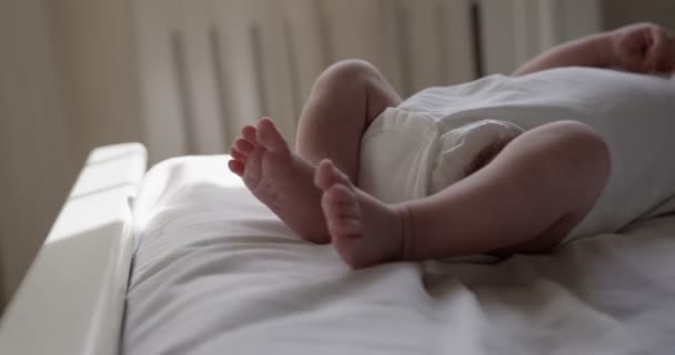 白い服を着た新生児の少年が白いベッドシートの上に腰を下ろしている 屋内で撃たれて閉じられた — ストック動画