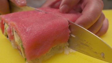 Making sushi rolls. Chief is cutting ready two sushi roll at once using chiefs knife. Closeup.