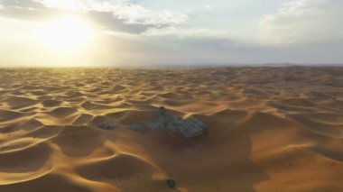 The flight of a drone around a lonely rock among the sandy desert against the backdrop of sunset