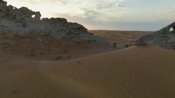 無人機は日没の空を背景に岩のために砂を登る男を撃つ — ストック動画