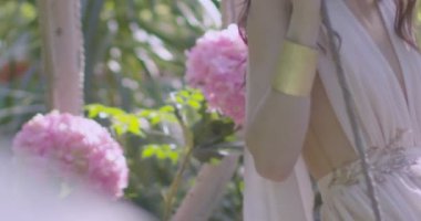 A young beautiful girl in a wreath of flowers swings on a swing among a green garden. Slow motion