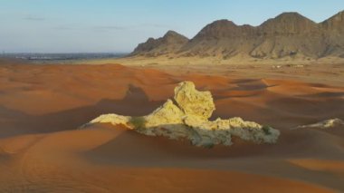 The flight of a drone around a lonely rock among the sandy desert against the backdrop of sunset