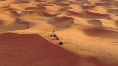 Bir dron, Birleşik Arap Emirlikleri 'nde çölün kum tepelerinden geçen dört tekerlekli bisikletlerin üzerinden uçuyor. Hava görünümü