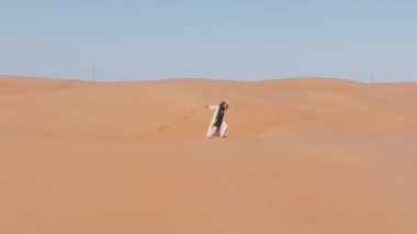 Çölde dans eden şaman gibi giyinmiş genç sakallı adam. İnsansız hava aracı