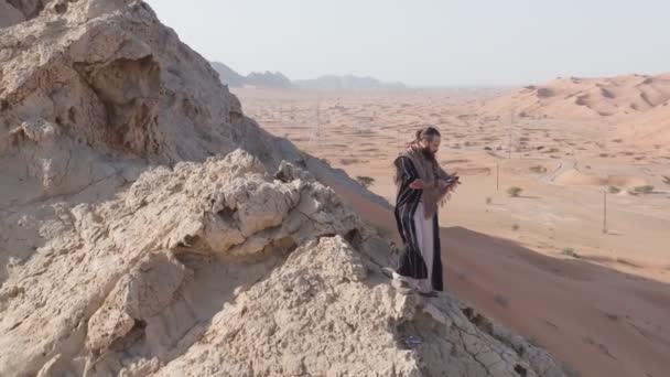 Homem Vestido Xamã Está Numa Pedra Meio Deserto Tem Telemóvel — Vídeo de Stock