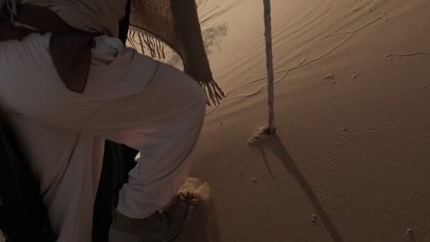 一个穿着白色萨满衣服 手里拿着手杖的年轻人 在日落的背景下走在沙漠的沙滩上 慢动作阿联酋 — 图库视频影像
