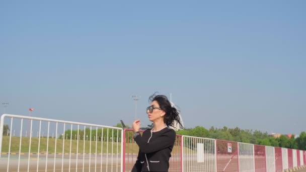 エレガントなドレスを着た若い女性が 飛行中のプライベートヘリコプターを背景に飛行場を歩く 澄んだ空 スローモーション — ストック動画