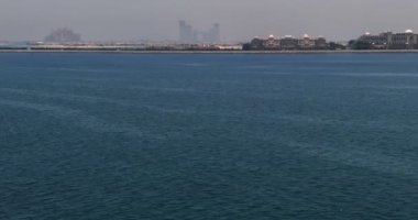 İnsansız hava aracı denizin dalgaları üzerinden kıyıdaki şehre doğru uçuyor. Dubai, Birleşik Arap Emirlikleri. Hava görünümü