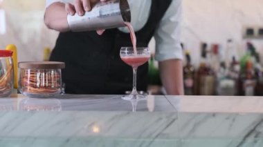 Pahalı bir otelde bir barmen bir bardaktan bardağa pembe bir kokteyl doldurur ve bir dilim limonla süsler. Kapat, Yavaş Hareket.