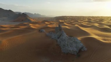 The flight of a drone around a lonely rock among the sandy desert against the backdrop of sunset