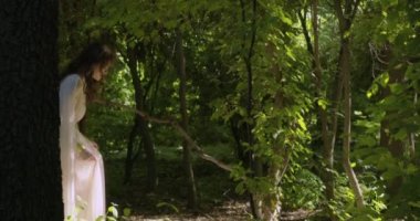 A young girl runs through a summer flowering garden among the trees in a light white fluttering dress. Slow motion