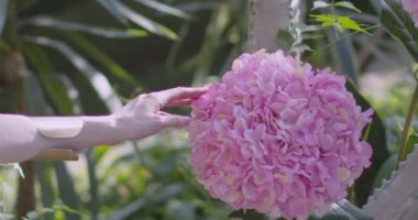 A young beautiful girl in a wreath of flowers swings on a swing among a green garden. Slow motion