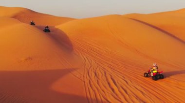 Bir dron, Birleşik Arap Emirlikleri 'nde çölün kum tepelerinden geçen dört tekerlekli bisikletlerin üzerinden uçuyor. Hava görünümü