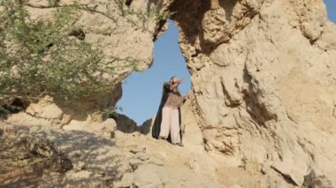 Genç sakallı bir şaman çölün kum tepelerinin arasında bir kaya mağarasında dururken dua eder. Yavaş çekim