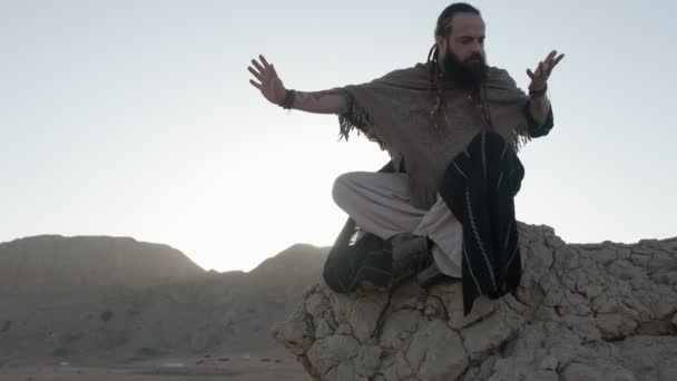 一个年轻的萨满在荷花的位置 在落日的背景下 在沙漠的沙丘中 在岩石上祈祷 慢动作 阿联酋 — 图库视频影像