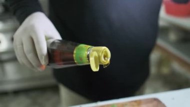 Beyaz eldivenli bir aşçı kesme tahtasına doğranmış ve karışık sebzelerden oluşan bir şişeden yağ döker. Kapat, Yavaş Hareket.