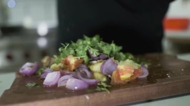Beyaz eldivenli bir şef kesim tahtasındaki doğranmış sebzelerin üzerine el değirmeninden biber serpiyor. Kapat, Yavaş Hareket.