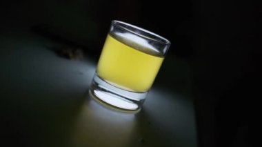 Bir bardak zeytinyağı, karanlık bir masanın üzerinde, arkada aydınlatılmış. Yavaş Hareket, Kapat.