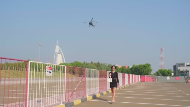 エレガントなドレスを着た若い女性が飛行場を通って高価なリムジンに向かいますプライベートヘリコプターの飛行を背景に 澄んだ空 スローモーション — ストック動画