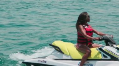 Açık denizlerde jet ski üzerinde can yeleği giymiş esmer bir kadın. Yavaş çekim