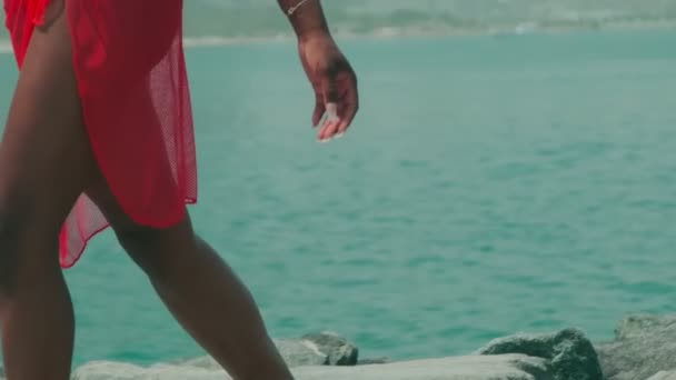 ビキニ姿の若い女と赤いドレスがドバイの海と高層ビルを背景に岩の上を裸足で歩く アラブ首長国連邦 スローモーション — ストック動画