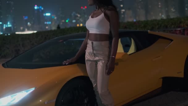 ヒールの高い靴を履いた若いエレガントな女性は 夜に高価なスポーツイエローの車の隣に立っています スローモーション — ストック動画