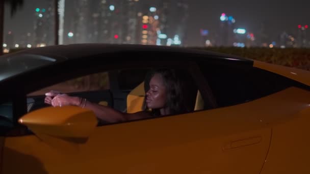 若いエレガントなSwarthy女性は高価なスポーツ黄色の車の車輪の後ろの夜に座っている 閉じる スローモーション — ストック動画