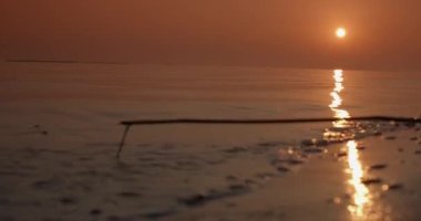 Gün batımında gölde sığ bir dalga sahilin kumlu sahiline yuvarlanır. Yakın çekim, gerçek zamanlı, 4K.