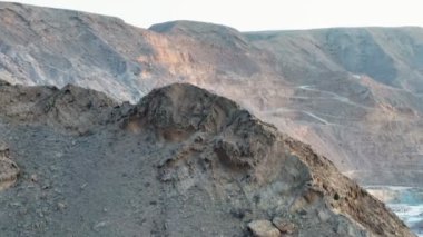 Kumlu çölün ortasında, batan güneşin arka planına karşı bir dronun kayalık bir tepenin üzerinden uçuşu.