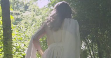 A young girl runs through a summer flowering garden among the trees in a light white fluttering dress. Slow motion