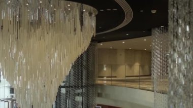 Gece elbisesi giymiş esmer genç bir kadın, merkezinde şık bir avize olan özel bir otelin lobisinde yürüyor. Yavaş Hareket