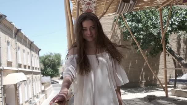 一位头发飘扬的年轻女子穿着白色的太阳衣 在芦苇树冠下走过一座古城 乌兹别克斯坦慢动作 — 图库视频影像