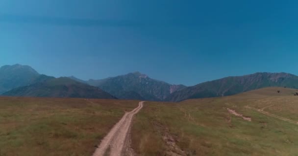 一架无人驾驶飞机飞越山坡上的一条土路 旁边是一座被群山环绕的湖泊 空中景观 慢动作 — 图库视频影像