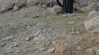 Elinde asa olan genç sakallı bir şaman çölün ortasındaki kayalıklarda yürüyor. Ağır çekim, BAE