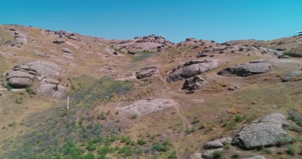 無人機は雲のない日に山に囲まれた岩の多い丘の上を飛ぶ 空中ビュー スローモーション — ストック動画