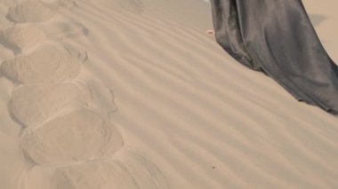 Young woman with long hair in an elegant black dress walking barefoot on the sand dunes of the desert. Slow Motion