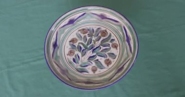 Paçavra arka planında seramikçi bir sanatçının stüdyosundaki desenlerle boyanmış porselen bir tabağın rotasyonu. Gerçek zamanlı, 4k.